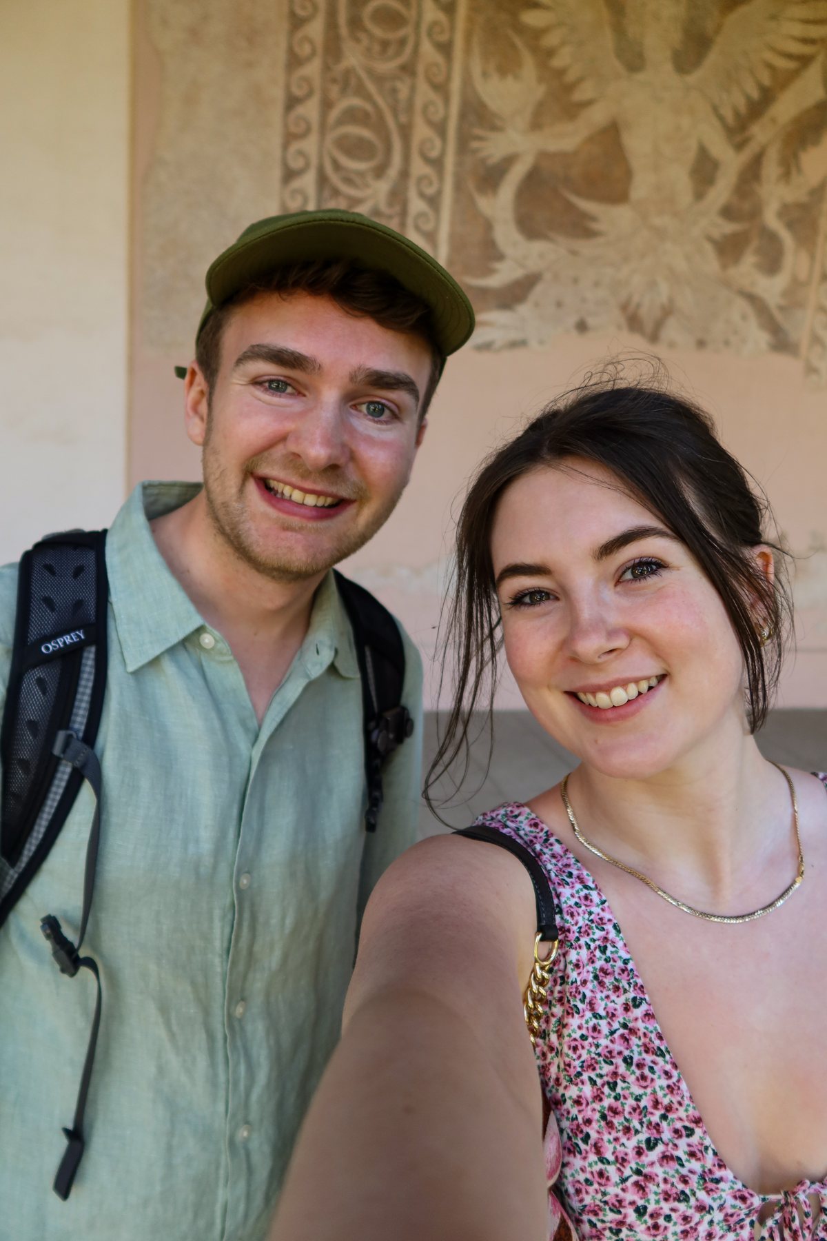 Ellie and Sam smiling in front of an ornate wall